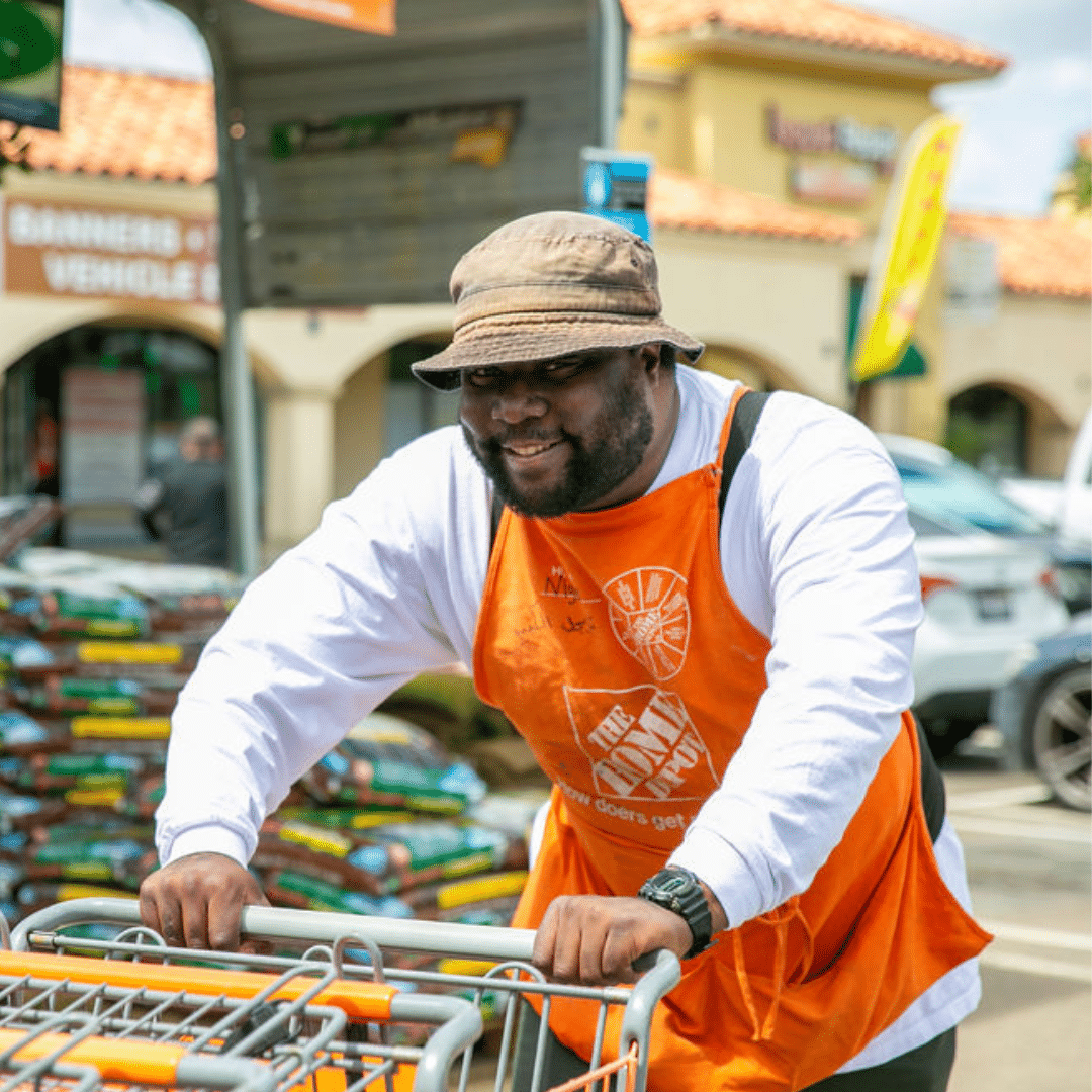 Picture of Home Depot employee in orange apron pushing carts in parking lot.